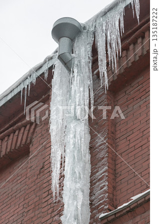 Closeup of drainpipe of building covered with thick layer of ice and icicles 135187222
