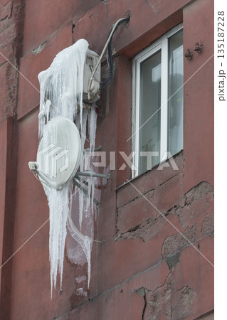 Satellite receiver dish on wall covered with icicles. Satellite receiver dish on wall covered with icicles. 135187228