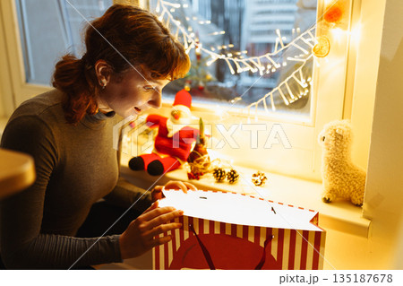 Young girl with gift box near christmas tree at home Young girl with gift box near christmas tree at home 135187678