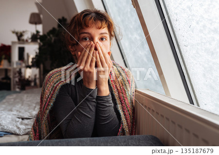 young woman warms herself near radiator at home in winter weather. young woman warms herself near radiator at home in winter weather. 135187679