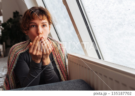 young woman warms herself near radiator at home in winter weather. young woman warms herself near radiator at home in winter weather. 135187702
