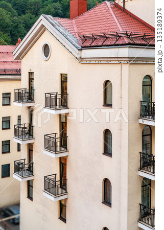 Modern residential building with beige facade , multiple balconies and red roof, Urban architecture with clean lines and neutral colors, suitable for real estate and city living concepts 135189374
