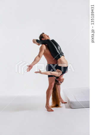 Strong athletic man lifting flexible woman in an extreme acrobatic contortion pose on a white background. Strong athletic man lifting flexible woman in an extreme acrobatic contortion pose on a white background. 135189431