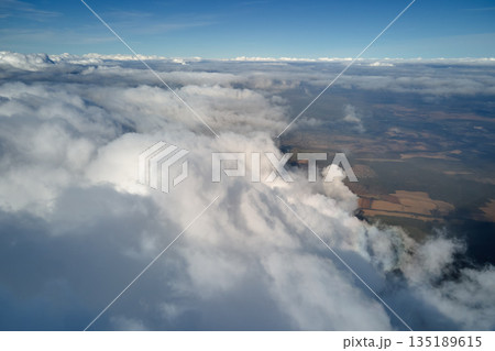 Aerial view from airplane window at high altitude of earth covered with puffy cumulus clouds forming before rainstorm Aerial view from airplane window at high altitude of earth covered with puffy cumulus clouds forming before rainstorm 135189615