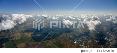 Aerial view from airplane window at high altitude of distant city covered with white puffy cumulus clouds. 135189616