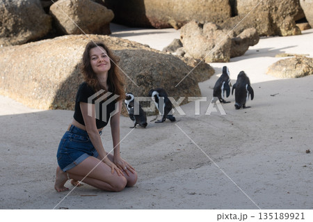 Tourist kneeling on Boulders Beach interacting with african penguins 135189921