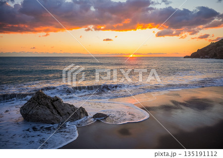 Orange Sunset Over Sea with Waves Hitting Rock Orange Sunset Over Sea with Waves Hitting Rock 135191112