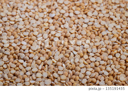 Yellow split peas close up revealing coarse groats texture, rustic pantry mood, warm beige tones, scattered pattern ideal for ingredient photography and recipe concept 135191435