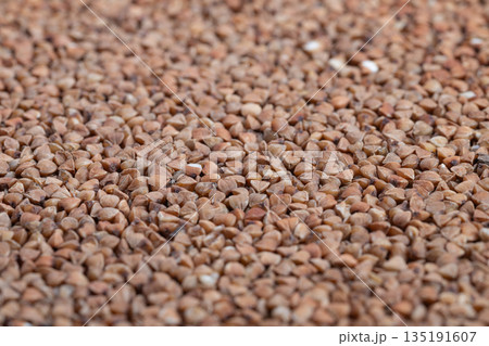 Pantry bulk buckwheat groats ready for storage and meal prep, coarse kernels filling container, warm brown hues suggesting longterm staple, ideal for supermarket and recipe imagery 135191607