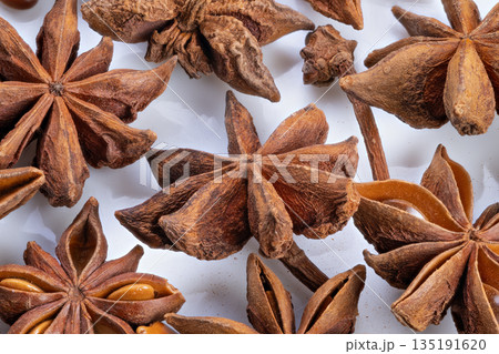 Close shot showcasing star anise texture and color, Detailed photograph capturing intricate textures and warm earthy tones of star anise pods on plain background 135191620