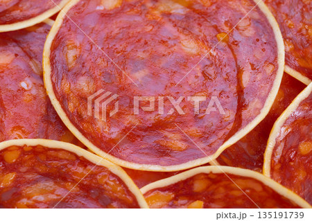 Spicy meat slices, Closeup of seasoned chorizo slices with cheese and paprika shine, Detailed view of overlapping spicy sausage rounds with cheese on textured surface 135191739