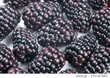 Highcontrast macro image of fresh glossy blackberries, Detailed macro photograph showcasing shiny blackberries on white background for marketing and culinary use Highcontrast macro image of fresh glossy blackberries, Detailed macro photograph showcasing shiny blackberries on white background for marketing and culinary use 135191993