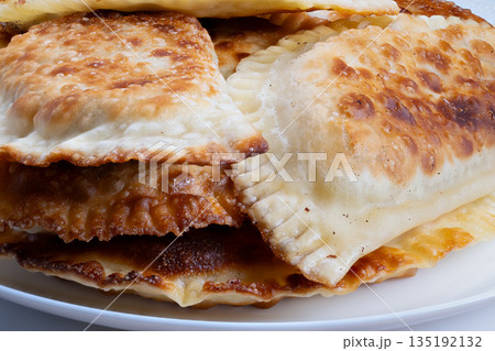 Warm crispy chebureki platter, Golden fried chebureki with filling on plate, Delicious golden fried chebureki stacked on plate showcasing rustic crust and hearty filling 135192132