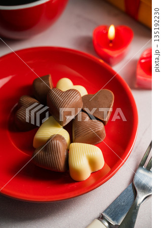 Valentine's Day chocolate candies in red plate served with a cup of coffee and candles 135192230