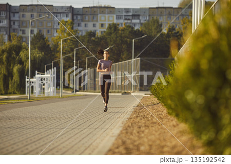Young woman runner on urban park path, morning fitness jogging and wellness 135192542