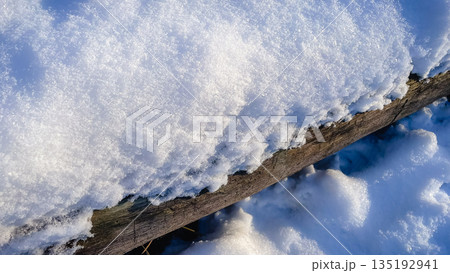 A thick layer of fresh white snow covers a rustic wooden beam on a sunny winter day A thick layer of fresh white snow covers a rustic wooden beam on a sunny winter day 135192941