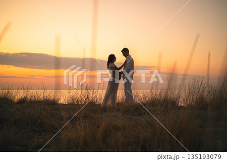 Pregnant Couple Embracing Sunset Bliss by the Ocean Pregnant Couple Embracing Sunset Bliss by the Ocean 135193079