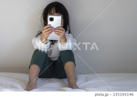 うす暗い部屋で座ってスマートフォンを見る女の子のイメージ(5歳、日本人、顔無し) うす暗い部屋で座ってスマートフォンを見る女の子のイメージ(5歳、日本人、顔無し) 135193146