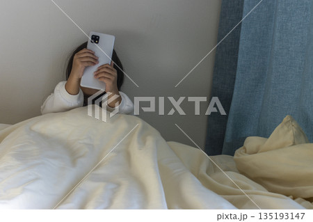 うす暗い部屋で座ってスマートフォンを見る女の子のイメージ（5歳、日本人、顔無し） 135193147