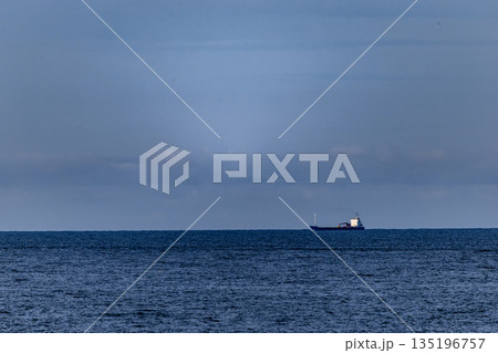 Distant Cargo Ship Against Expansive Ocean and Tranquil Sky 135196757