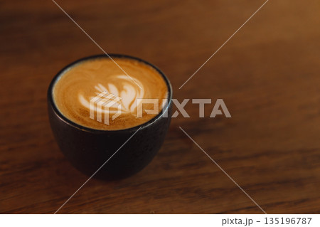 Latte Art Cappuccino in Black Cup on Warm Wooden Table Surface 135196787