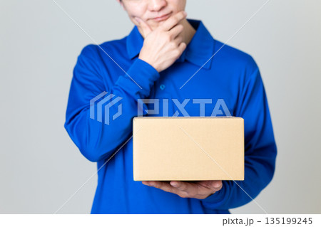 段ボールの荷物を持って悩む物流・運送業の男性 135199245