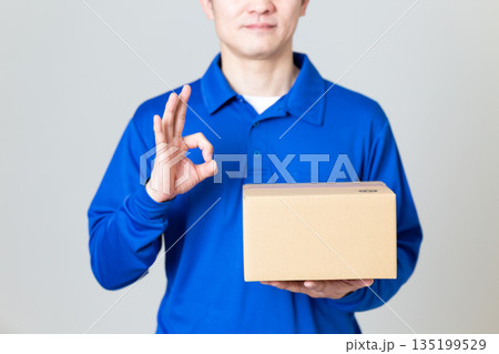 段ボールの荷物を持って丸のポーズをする物流・運送業の男性 135199529