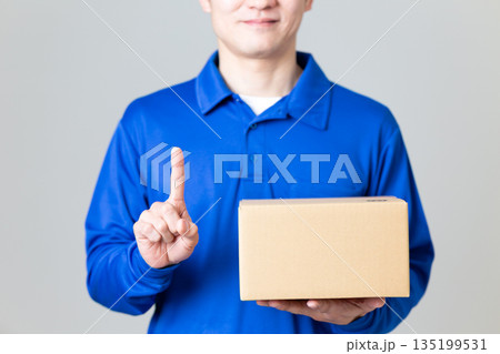 段ボールの荷物を持って人差し指を立てる物流・運送業の男性 135199531