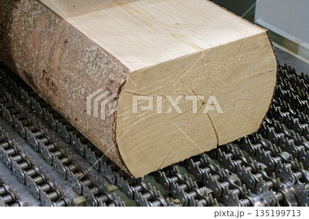 Partially processed log on the conveyor of a woodworking machine 135199713