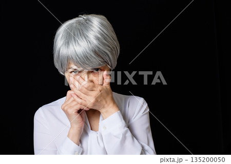 口元を抑え睨みつけるブラウスを着た白髪のシニア女性 135200050