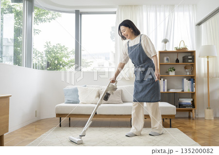 リビングルームで掃除機をかける50代の女性 リビングルームで掃除機をかける50代の女性 135200082