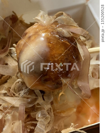 Takoyaki, a popular Japanese street food, are crispy round dough balls filled with octopus, tempura bits, and pickled ginger, topped with takoyaki sauce, bonito flakes, and aonori. 135200528