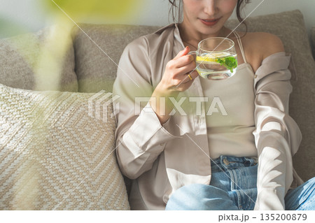 ソファーに座りレモン水,デトックスウォーターを飲む女性 ソファーに座りレモン水,デトックスウォーターを飲む女性 135200879