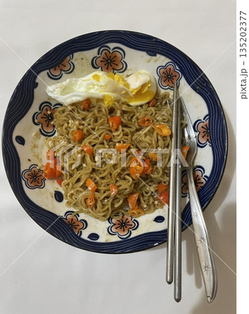 Indomie goreng, a popular Indonesian instant noodle dish, stir-fried to perfection with a blend of savory seasonings. Often served with fried egg, crispy shallots, and vegetables for flavor Indomie goreng, a popular Indonesian instant noodle dish, stir-fried to perfection with a blend of savory seasonings. Often served with fried egg, crispy shallots, and vegetables for flavor 135202377