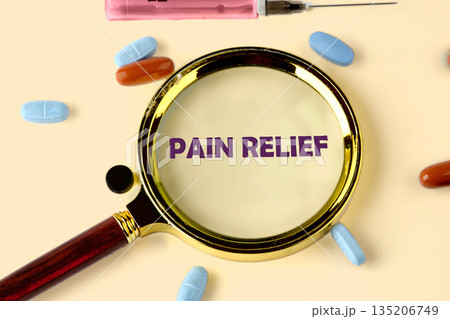 Purple text reading PAIN RELIEF is magnified by a golden-rimmed magnifier. Blue and brown pills and a pink syringe are situated on a pale surface, suggesting medication 135206749