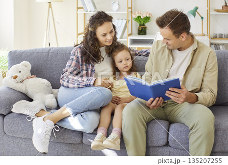 Happy family reading a storybook together on the sofa at home, playful moments 135207255
