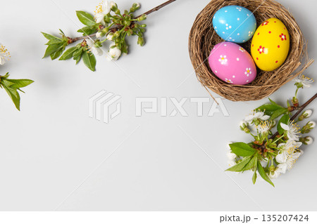 Easter colored painted eggs in bird nests and blooming spring cherry branches on gray background in shape of frame with space for text and greetings. Easter and spring concept. Spring background Easter colored painted eggs in bird nests and blooming spring cherry branches on gray background in shape of frame with space for text and greetings. Easter and spring concept. Spring background 135207424