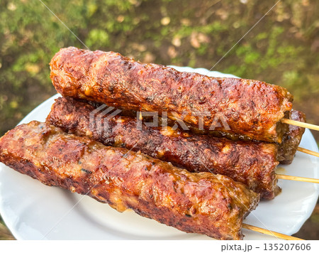 Grilled kebabs on skewers served on a plate outdoors. 135207606