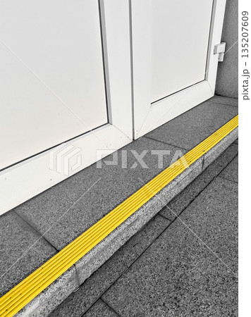 Entrance with yellow safety strip on tiled floor. 135207609