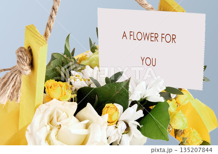 A bouquet of radiant yellow and white flowers nestles inside a bright yellow holder. A simple white card reads A Flower For You, offering a heartfelt gift 135207844