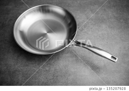 Modern stainless steel pan with textured background and dramatic lighting, Elegant cookware featuring smooth handle set against patterned surface with intense contrast effects Modern stainless steel pan with textured background and dramatic lighting, Elegant cookware featuring smooth handle set against patterned surface with intense contrast effects 135207928