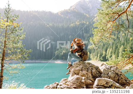 Back view young woman with backpack looking the view of the mountain lake in sunny weather. 135211198