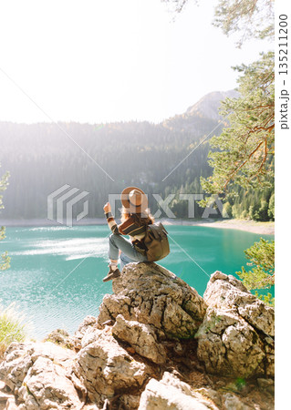 Young woman traveler enjoys fresh air and a beautiful view of the lake and mountains. Active life 135211200