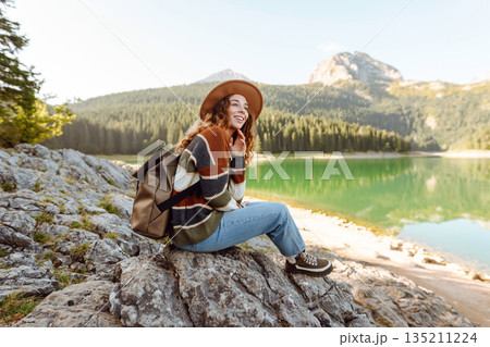Young woman traveler enjoys fresh air and a beautiful view of the lake and mountains. Active life 135211224