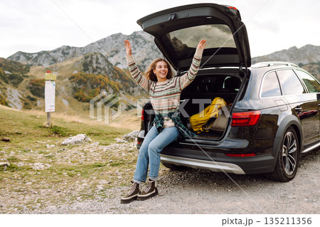 Young woman enjoying autumn nature while sitting in trunk of her car during a solo trip. Road trip Young woman enjoying autumn nature while sitting in trunk of her car during a solo trip. Road trip 135211356