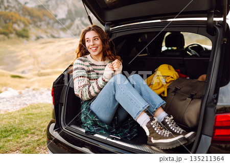 Young woman enjoying autumn nature while sitting in trunk of her car during a solo trip. Road trip 135211364