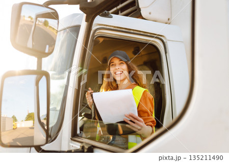 Portrait of beautiful young woman professional truck driver checking shipment list on a -parking lot Portrait of beautiful young woman professional truck driver checking shipment list on a -parking lot 135211490