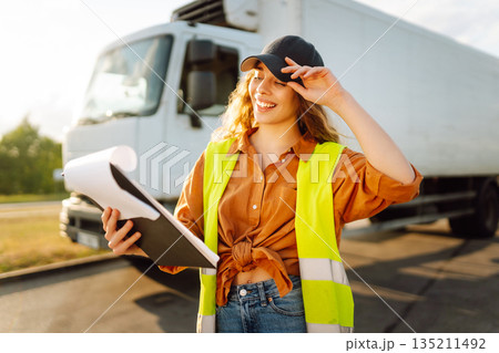Portrait of beautiful young woman professional truck driver checking shipment list on a -parking lot 135211492