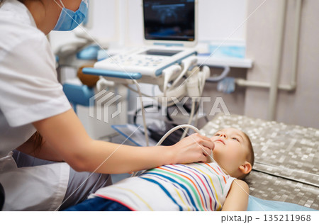 Boy undergoing thyroid ultrasound examination. Doctor examining kid throat in clinic with equipment. Boy undergoing thyroid ultrasound examination. Doctor examining kid throat in clinic with equipment. 135211968