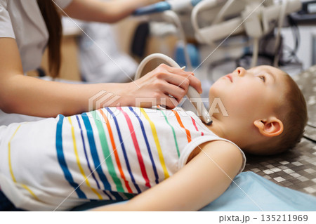 Boy undergoing thyroid ultrasound examination. Doctor examining kid throat in clinic with equipment. 135211969